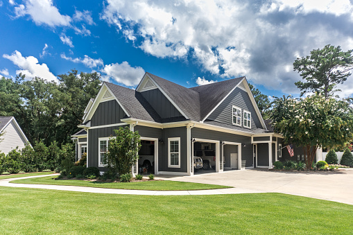 The side view of a large gray craftsman new construction house with a landscaped yard a three car garage and driveway