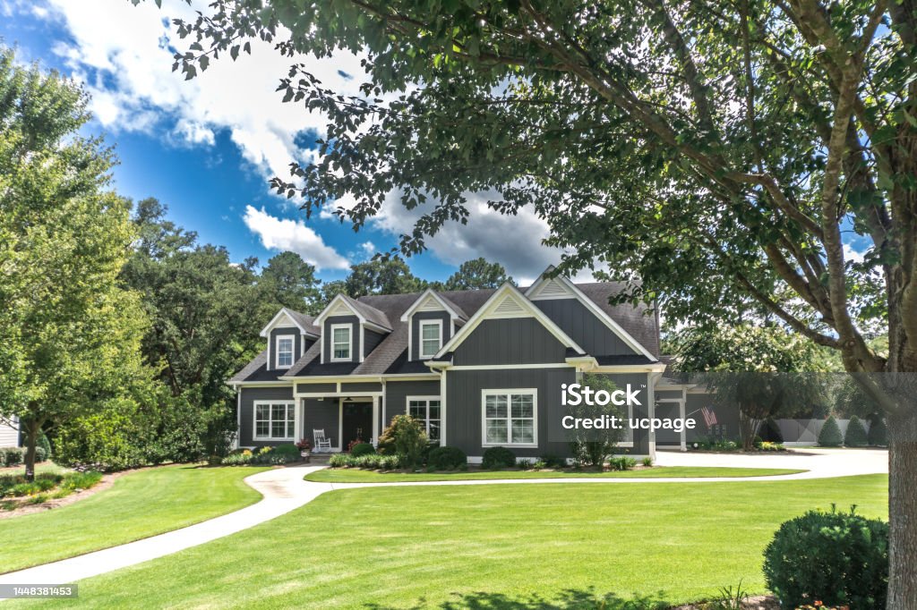 A large gray craftsman new construction house with a landscaped yard and leading pathway sidewalk A large gray craftsman new construction house with a landscaped yard and leading pathway sidewalk on a sunny day with blue skies and clouds. Residential Building Stock Photo