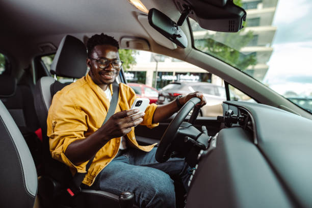 Happy young African-American man driving a car and using smart phone stock photo