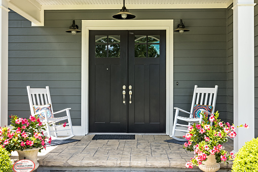 A front porch with two rocking chairs, stamped concrete floors, and double glass doors.