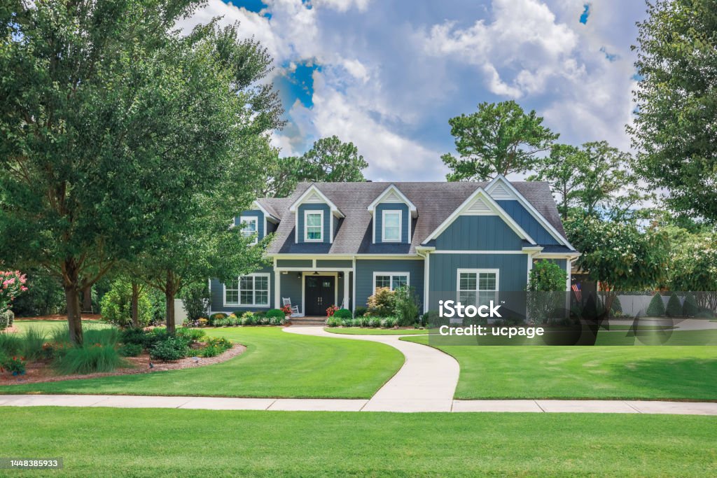 A large blue craftsman new construction house with a landscaped yard and leading pathway sidewalk A large blue craftsman new construction house with a landscaped yard and leading pathway sidewalk on a sunny day with blue skies and clouds. House Stock Photo