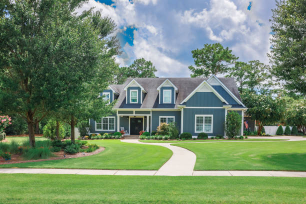 A large blue craftsman new construction house with a landscaped yard and leading pathway sidewalk A large blue craftsman new construction house with a landscaped yard and leading pathway sidewalk on a sunny day with blue skies and clouds. blue house stock pictures, royalty-free photos & images