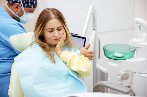 Young woman feeling pain, holding her cheek with hand at dentist's office.Toothache concept.