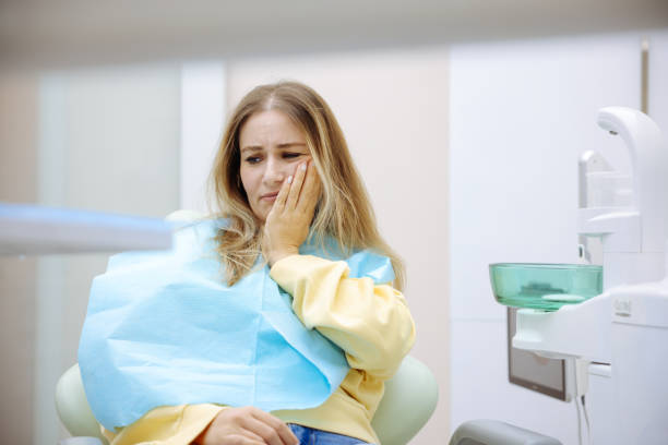 歯科医院で手で頬を押さえ、痛みを感じる若い女性。歯痛のコンセプト。 - dentists chair 写真 ストックフォトと画像