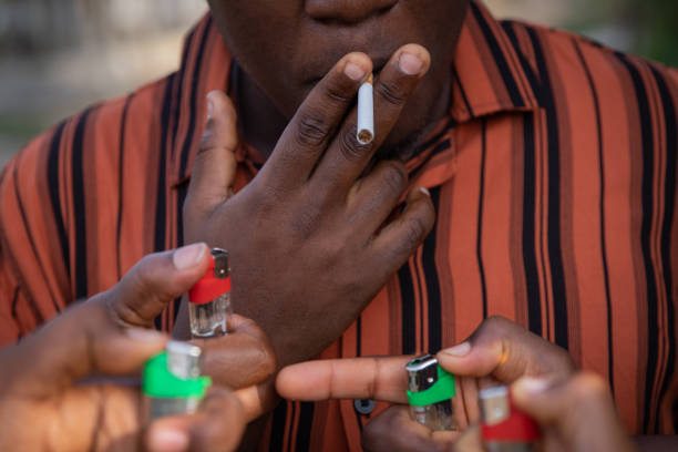 A man with a cigarette in his mouth while hands with lighters want to light the cigarette. A man with a cigarette in his mouth while hands with lighters want to light the cigarette anti tobacco day stock pictures, royalty-free photos & images