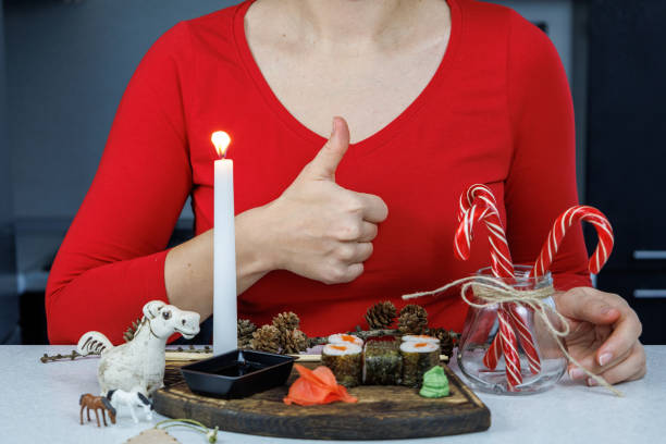 Japanese rolls with red fish on a wooden cutting board. A girl in a red sweater eats sushi with chopsticks. Table decoration with candles and sweets. Christmas concept Japanese rolls with red fish on a wooden cutting board. A girl in a red sweater eats sushi with chopsticks. Table decoration with candles and sweets. Christmas concept. kids eating tuna stock pictures, royalty-free photos & images