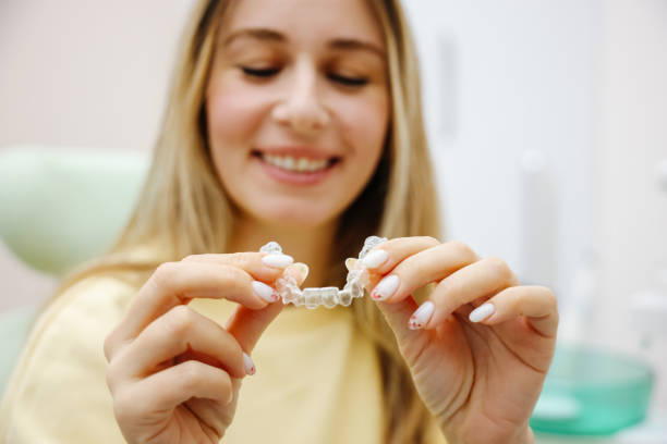 Dental invisible braces or silicone trainer in the hands of a young smiling women. Orthodontic concept - Invisalign Smiling beautiful Caucasian mid adult woman holding invisible orthodontic retainer dental equipment hand stock pictures, royalty-free photos & images