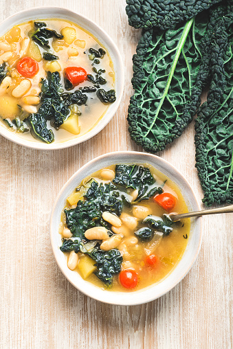 Black cabbage (Toscan kale or cavolo nero) Minestrone soup  with white Cannellini beans on the wooden background. Italian Tuscan Medici winter recipes. Healthy  tradition vegetarian food