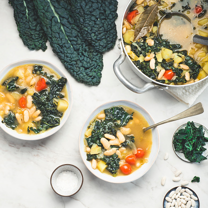 Black cabbage (Toscan kale or cavolo nero) Minestrone soup  with white Cannellini beans on the white background. Italian Tuscan Medici winter recipes. Healthy  tradition vegetarian food, square crop