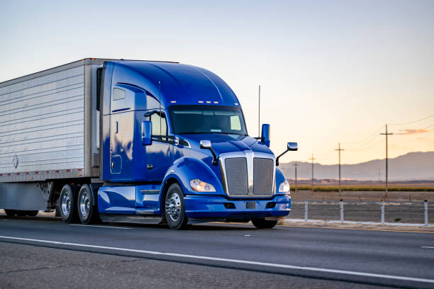 Bright blue powerful big rig semi truck transporting cargo in reefer semi trailer driving on the road with sunset stock photo