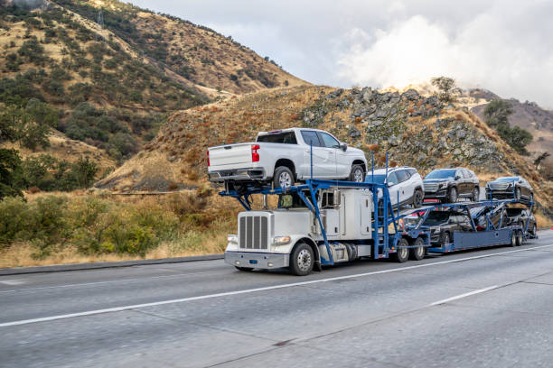 Classic powerful big rig car hauler semi truck transporting crossovers on the modular semi trailer climbing uphill on the multiline mountain highway road stock photo