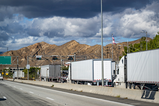 Convoy of industrial grade commercial transportation of different big rig semi trucks with semi trailers standing on the at the weighing station with scales for weighing along the axes in California