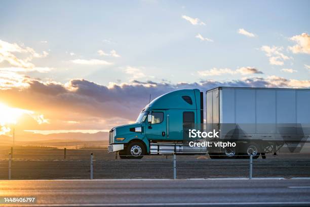 Streamline Green Big Rig Bonnet Semi Truck Transporting Cargo In Dry Van Semi Trailer Driving On The Highway Road With Fields On The Sides At Sunset Time Stock Photo - Download Image Now