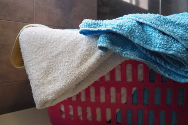 Towels in the laundry basket. Blue and pink cotton terry towels are thrown into a pink plastic basket. Housekeeping. Storing and separating laundry before washing. Light from above from open window. stock photo