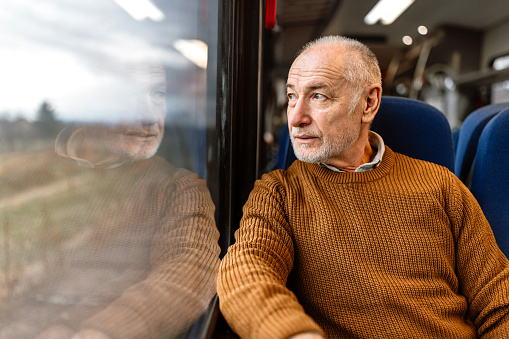 Senior handsome man traveling by train, sitting next to the window, looking at view, enjoying journey.