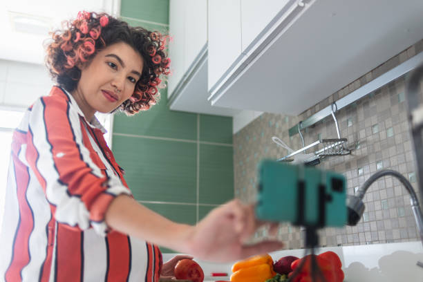 Young pregnant woman cutting vegetables while watching a video tutorial at the kitchen counter