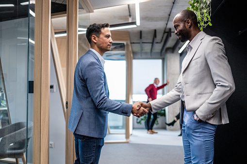 Two businessmen shaking hands while standing in an office space.