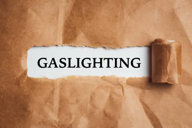 the word Gaslighting appearing behind torn brown paper.