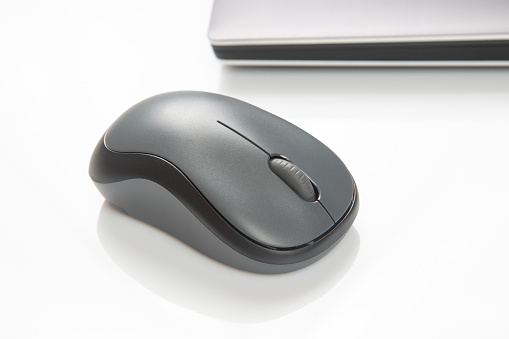 Computer wireless mouse next to a laptop on a white table close-up. electronic personal industry