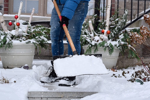 Man shoveling snow from the front yard walkway of a residential house, shovel with snow lifted up in the air