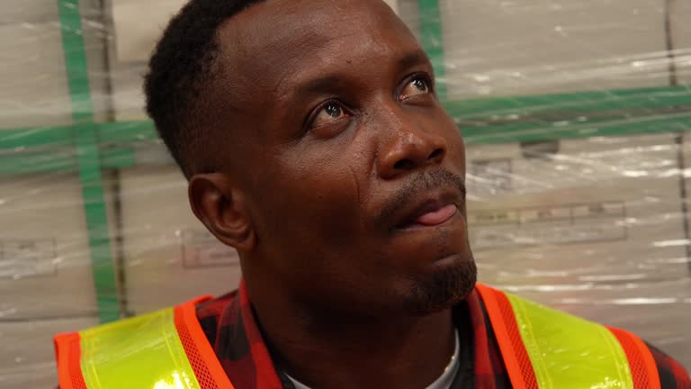 African worker man taking a break and eating hamburger  in warehouse store , licking lips