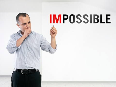 Businessman writing ‘impossible’ on transparent wipe board.
