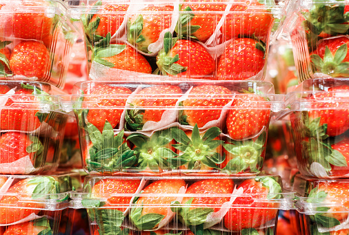 Stacks of fresh strawberries in plastic containers close up in a supermarket.