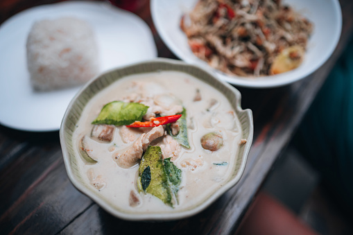 A plate of soup with coconut milk, boiled rice, and a tea leaf salad on the table.