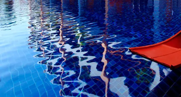 The pool has white reflections from above,with blue tiled floors in front of it with orange woodenboat