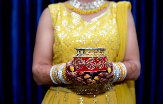 Young Indian woman celebrating Karwa Chauth at home. Karwa Chauth is a festival celebrated by Hindu women of Northern and Western India on the fourth day after Purnima in the month of Ashwin.