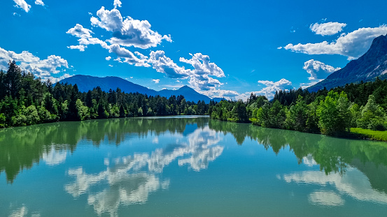 River Gail flowing through the Schuett in the natural park Dobratsch in Villach, Carinthia, Austria. Gailtaler and Villacher Alps. River gets very broad. Reflections in crystal clear water. Mountains