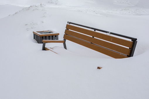 A bench in a city park completely covered with snow, winter weather snowfall, a bench hidden under a layer of snow