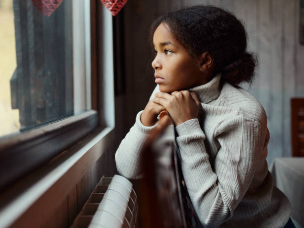istock Black girl looking through window from home. 1448454947