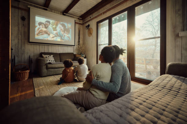 widok z tyłu zrelaksowanej czarnej rodziny oglądającej film w domu. - urządzenie projekcyjne zdjęcia i obrazy z banku zdjęć