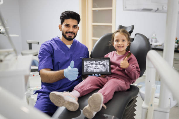 Caucasian preschool girl, sitting on dentist chair and looking at digital tablet with x-ray scan Pretty smiling preschool girl, sitting on dentist chair and looking at digital tablet with x-ray scan image of teeth together with her professional male bearded dentist at clinic showing thumbs up. tablet pc and digital hospital tools stock pictures, royalty-free photos & images