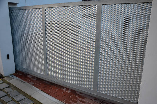 above the fence on the metal post by the entrance gate are two cameras with rotating lenses. they monitor who enters the building and who leaves. protection and records instead of a gatehouse, flash light, sliding gate entrada al patio al estacionamiento a través de una puerta corredera baja. la puerta se mueve lateralmente a lo largo del ferrocarril. hay una baliza intermitente naranja en el poste. el control remoto enciende la puerta corredera, sensor infrarrojo, meta