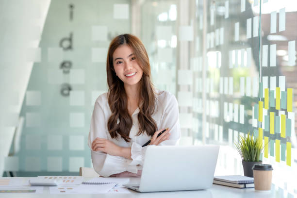 Beautiful smiling young Asian businesswoman sitting with arms crossed looking at camera in the office. stock photo