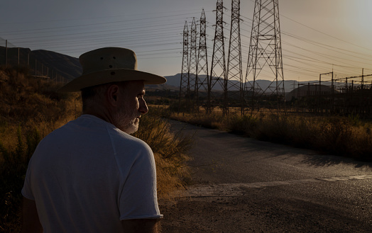 Rear view of adult man in cowboy hat against transmissions towers during sunset