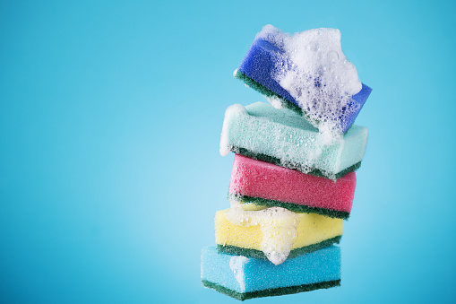 Stack of kitchen multi coloured sponges with detergent foam on blue background. Dish washing sponges.