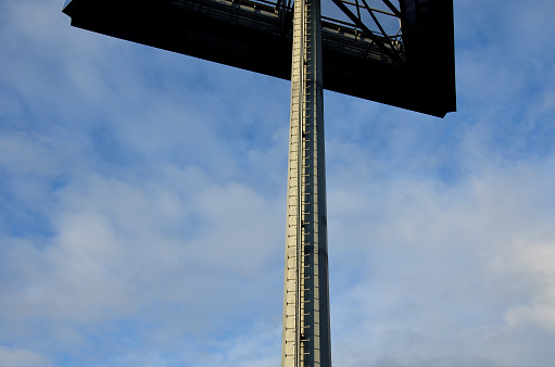 a ladder with free ends on a pole near an outdoor advertising area. rungs of the ladder, footboards fixed in the center of the tube. galvanized metal pillar surface, blue sky, winter, galvanized steel, pillar, subtle
