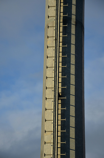 a ladder with free ends on a pole near an outdoor advertising area. rungs of the ladder, footboards fixed in the center of the tube. galvanized metal pillar surface, blue sky, winter, galvanized steel, pillar, subtle