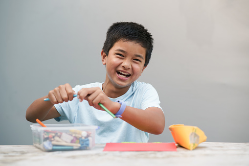 Active kid playing at home coloring with big smile looking at camera.