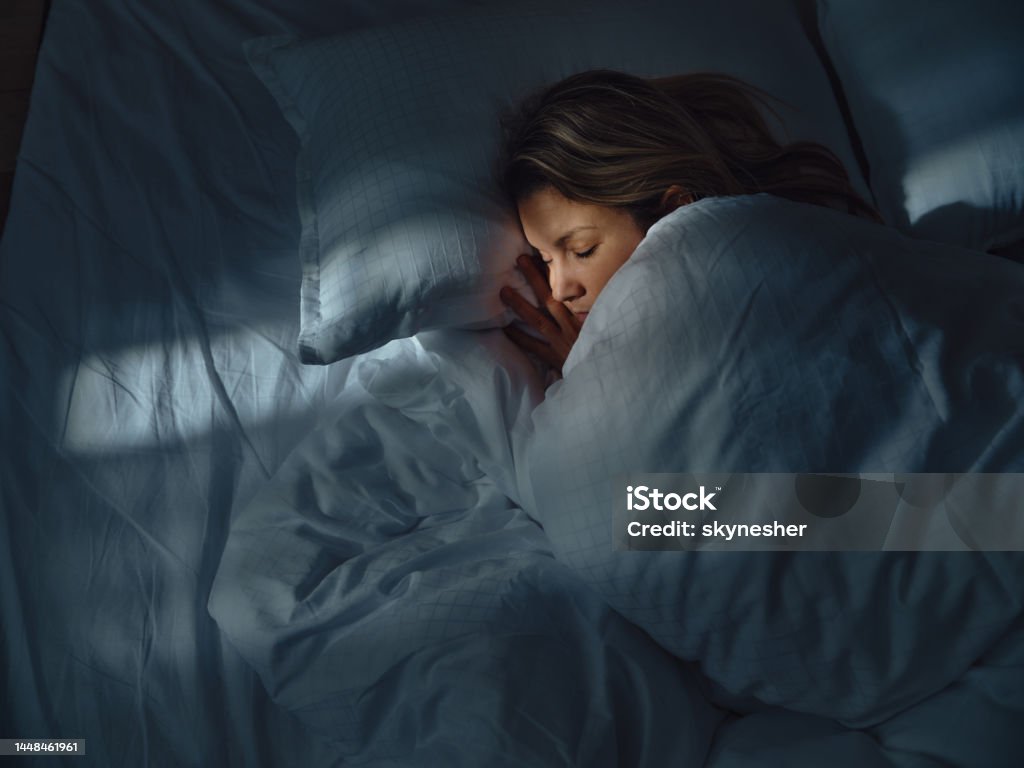 Above view of relaxed woman sleeping in bed at night. High angle view of a woman taking a nap in her bed at night. Photographed in medium format. Sleeping Stock Photo