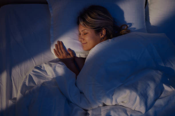 Above view of smiling woman sleeping in bed. High angle view of young woman smiling while dreaming in bed at night. only women women bedroom bed stock pictures, royalty-free photos & images