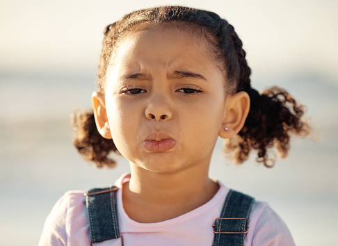 Portrait, sad and face of an unhappy little girl feeling lonely or upset against a blurred background. Closeup of an emotional African female child with depressed facial expression for end of summer