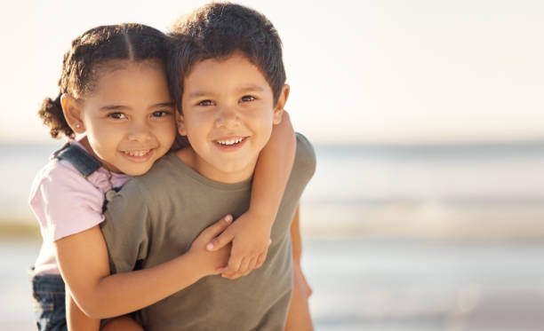 glücklich, lächeln und porträt von geschwistern am strand, die sich im sommerurlaub umarmen und spielen. glück, meer und bruder geben seiner schwester eine huckepackfahrt während eines familienurlaubs am meer. - buben stock-fotos und bilder