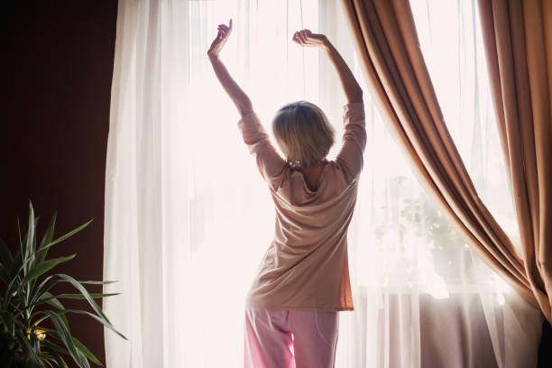 istock Happy middle aged woman sits on bed and stretching arms 1448468268