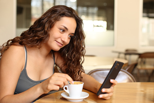Woman checking phone and stirring coffee in a bar