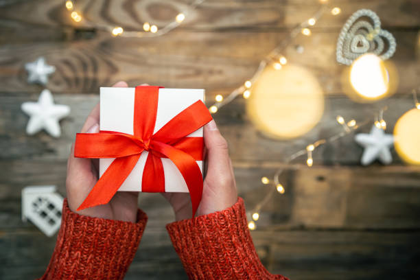 istock Gift box in female hands on a blurred background with bokeh, top view. 1448470936