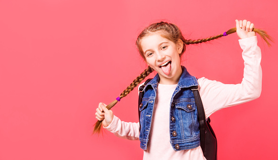 Portrait of smiling young little girl with two french braides on pink background